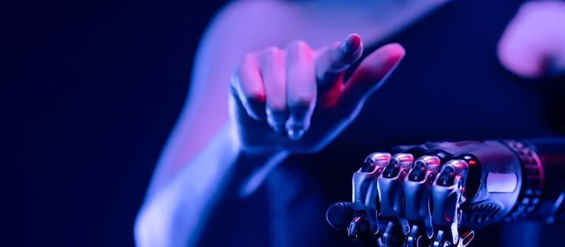 A woman holds a robotic hand emitting blue light, symbolizing the integration of AI and virtual assistance in technology.