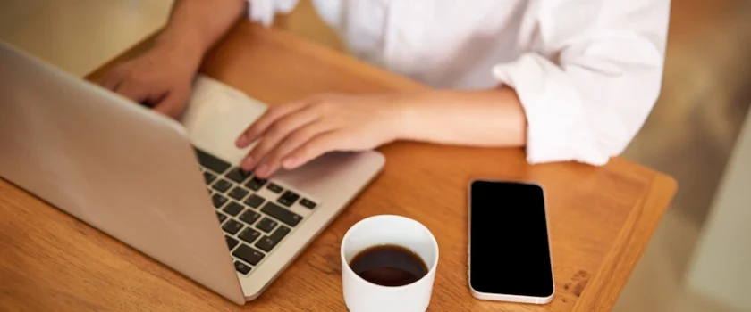 Virtual assistants working on a laptop next to a smartphone and a cup of coffee on a wooden table.