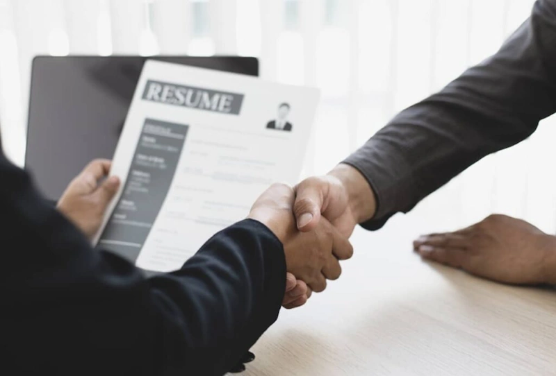 Two individuals shaking hands over a resume reflecting a reliable Hire Virtual Assistant Philippines service
