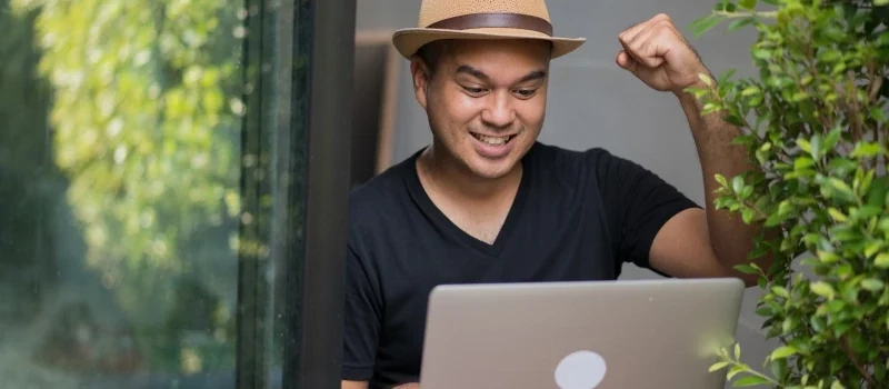 hire-your-SEO-virtual-assistant-man-smiling-and-raising-his-fist-while-using-a-laptop