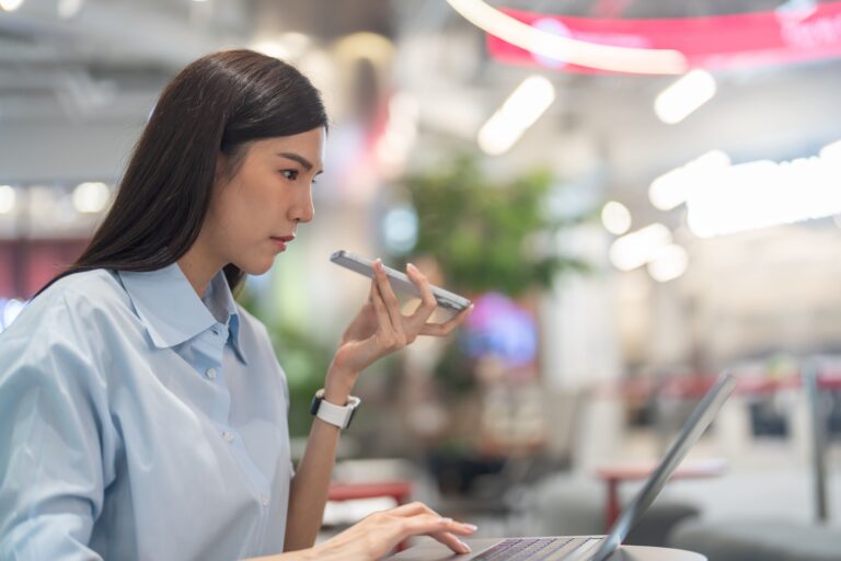 A skilled virtual assistant Philippines professional managing business tasks on her laptop while answering a voice message.